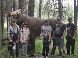 A group of people are standing in front of a moose statue in the woods.