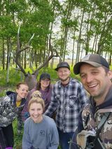 A group of people are posing for a picture in front of a deer in the woods.