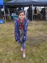 A little girl is standing in a field wearing rain boots and a medal.