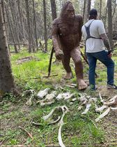 A man is standing next to a statue of a bigfoot in the woods.