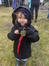 A little girl in a black jacket is holding a medal.