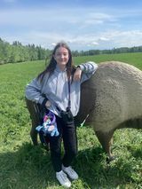 A girl is standing next to a pig in a field.