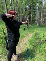 A woman is practicing archery in the woods.