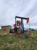 A group of people are standing on top of an oil pump in a field.