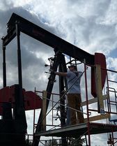 A man is standing on a scaffolding next to an oil pump.