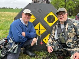 Two men are sitting next to each other in front of a target.