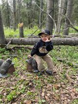 A little boy is standing next to a statue of a squirrel in the woods.