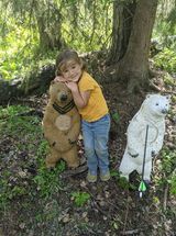 A little girl is standing next to two bear statues in the woods.