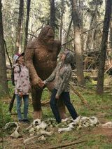 A woman is standing next to a statue of a bigfoot in the woods.