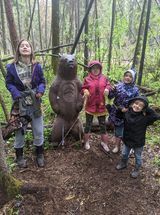 A group of children are standing next to a statue of a bear in the woods.