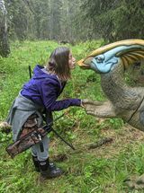 A woman is standing next to a dinosaur statue in a field.