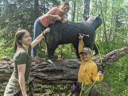 A group of people are standing next to a statue of a bear in the woods.