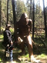 A man is standing next to a statue of a bigfoot in the woods.