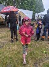 A little girl is standing in the rain under an umbrella.