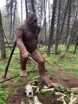 A statue of a bigfoot standing in the middle of a forest.
