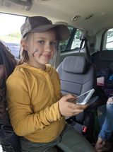 A young girl is sitting in the back seat of a car holding a cell phone.