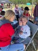 A woman is painting a little girl 's face at a festival.