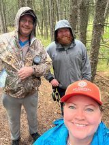 A woman is taking a selfie with two men in the woods.