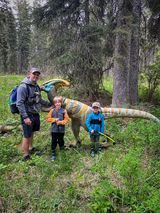 A man and two children are standing next to a dinosaur in the woods.
