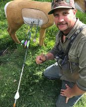 A man is kneeling down next to a deer target with arrows in it.