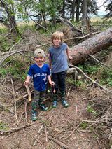 Two young boys are standing next to each other in the woods.