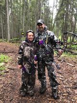 A man and a boy are standing in the woods holding bows and arrows.