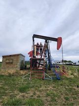 A group of people are standing on top of an oil pump in a field.