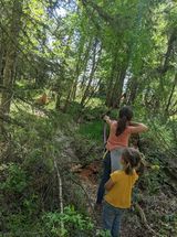 Two young girls are walking through a lush green forest.