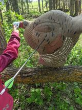 A person is holding an arrow in front of a target in the woods.