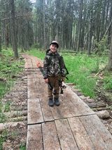 A young boy is standing on a wooden bridge in the woods.