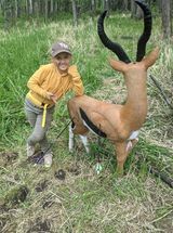 A young girl is standing next to a deer statue in a field.