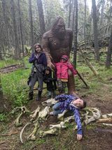 A family is standing next to a statue of bigfoot in the woods.