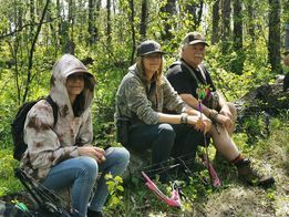 A group of people are sitting in the woods with bows and arrows.