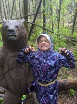 A young girl is standing next to a bear statue in the woods.