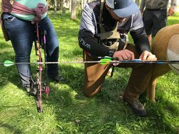 A man is kneeling down in the grass with an arrow in his hand.