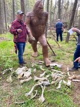 A man is standing next to a statue of a bigfoot in the woods.