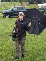 A young man is holding an umbrella and a fishing rod in a field.