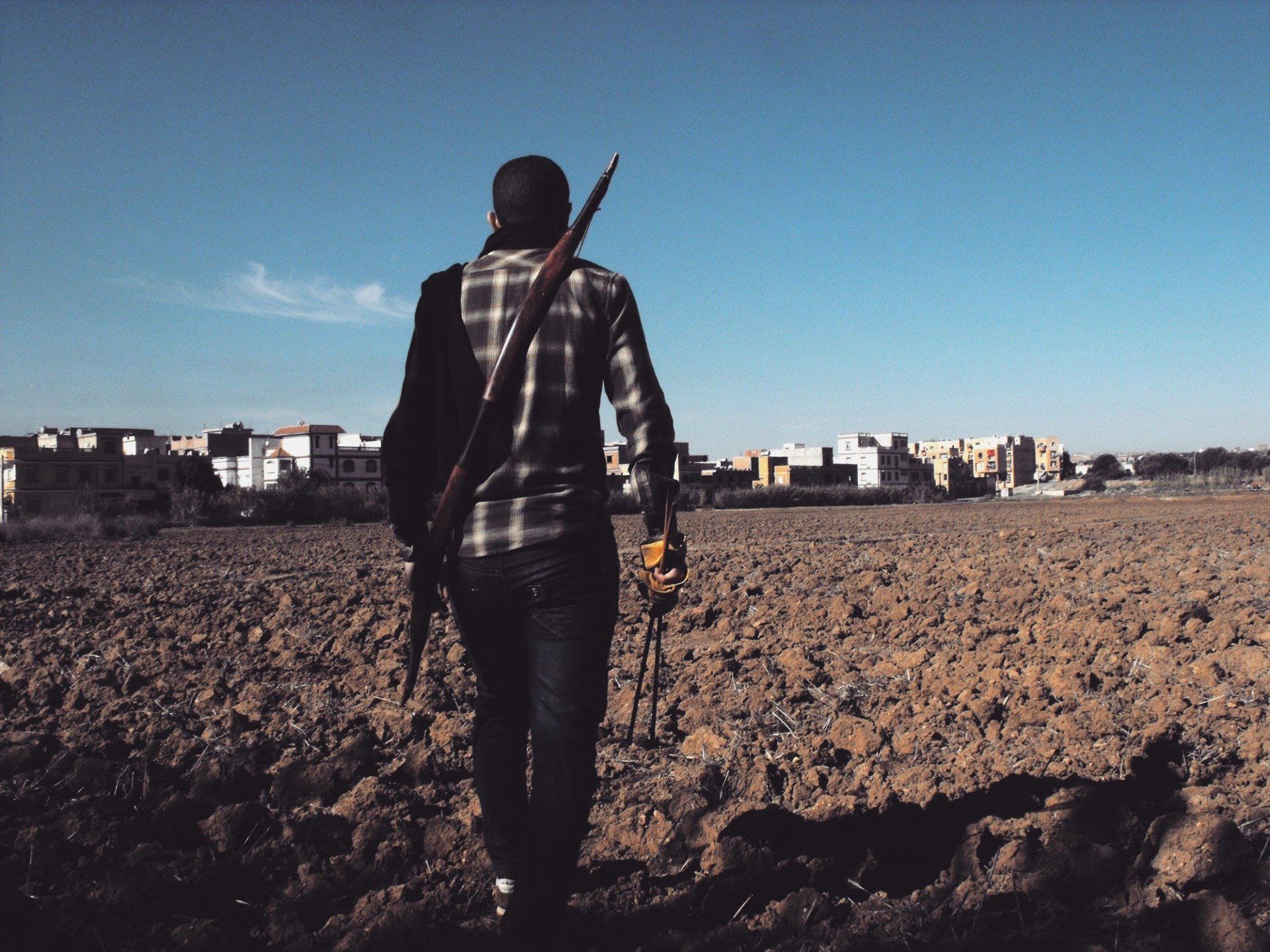 A man in a plaid shirt is walking through a dirt field