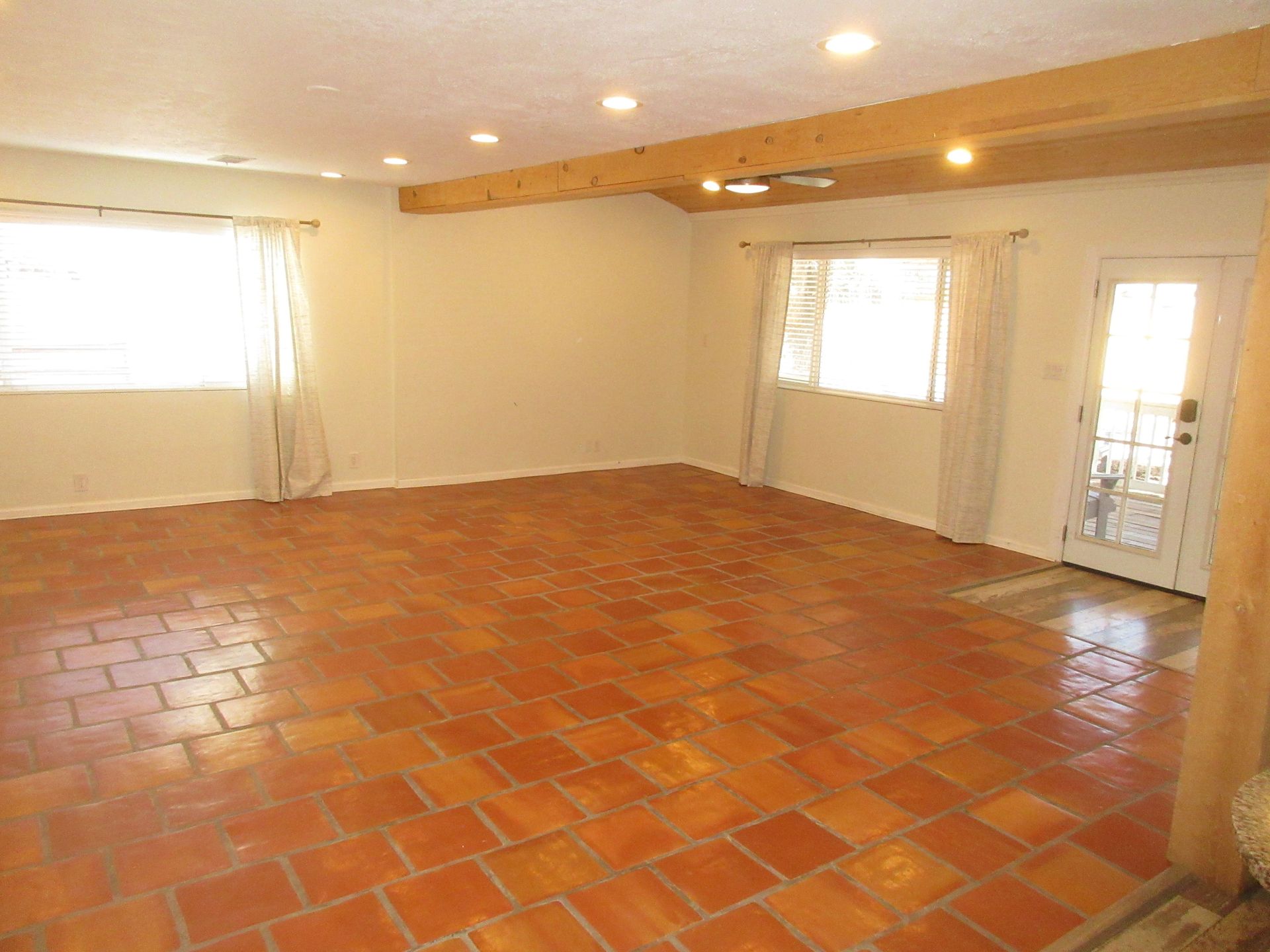 An empty living room with a tiled floor and two windows.