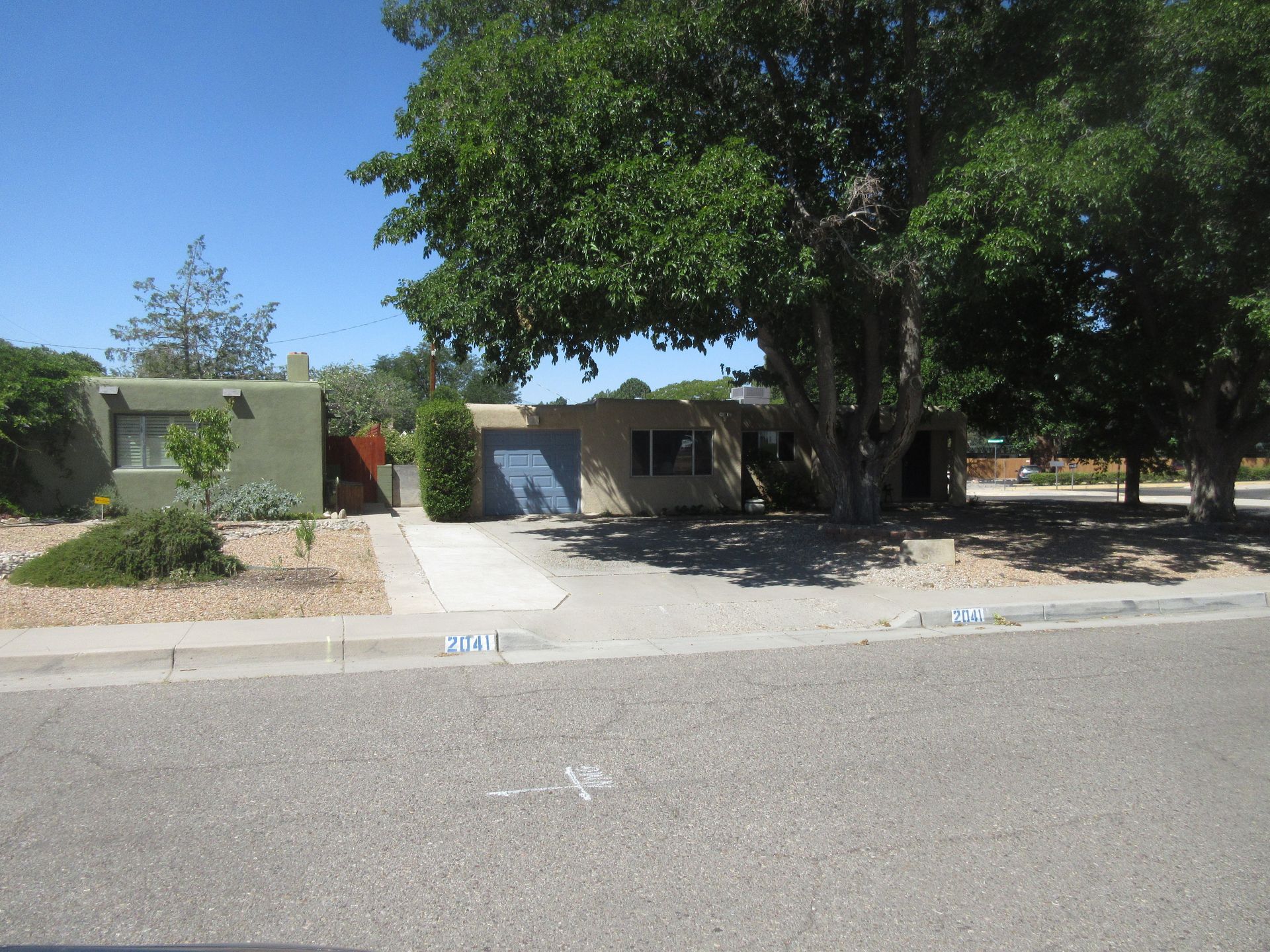 A house sits on the corner of a street with a tree in front of it