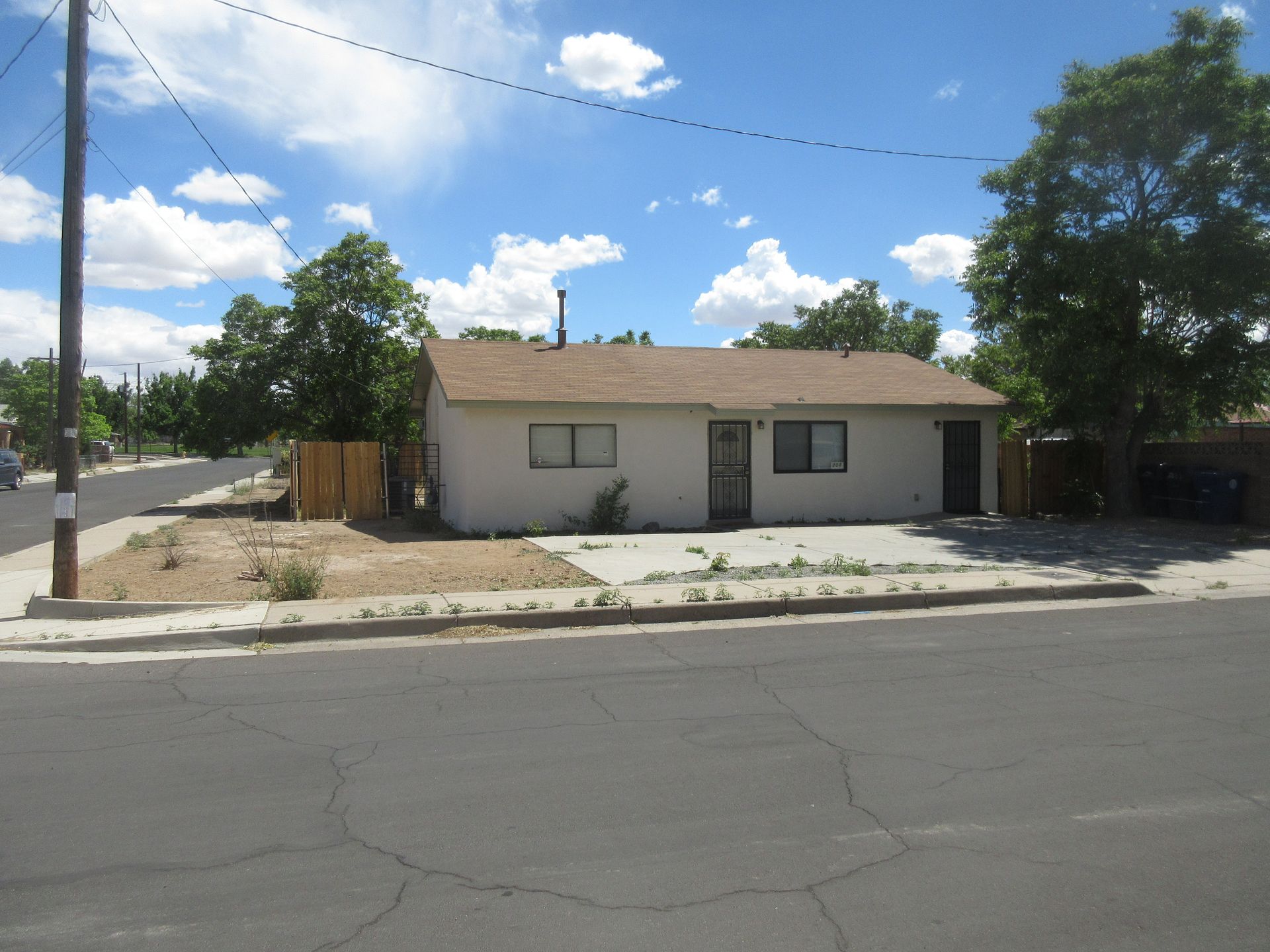 A white house with a brown roof sits on the corner of a street