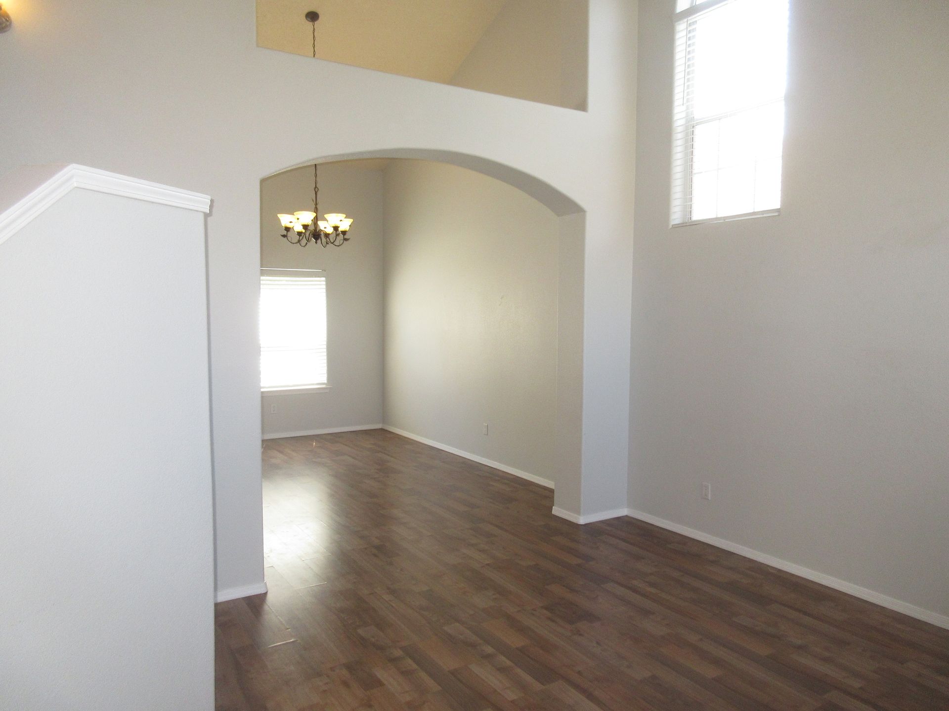 An empty living room with hardwood floors and a chandelier hanging from the ceiling.