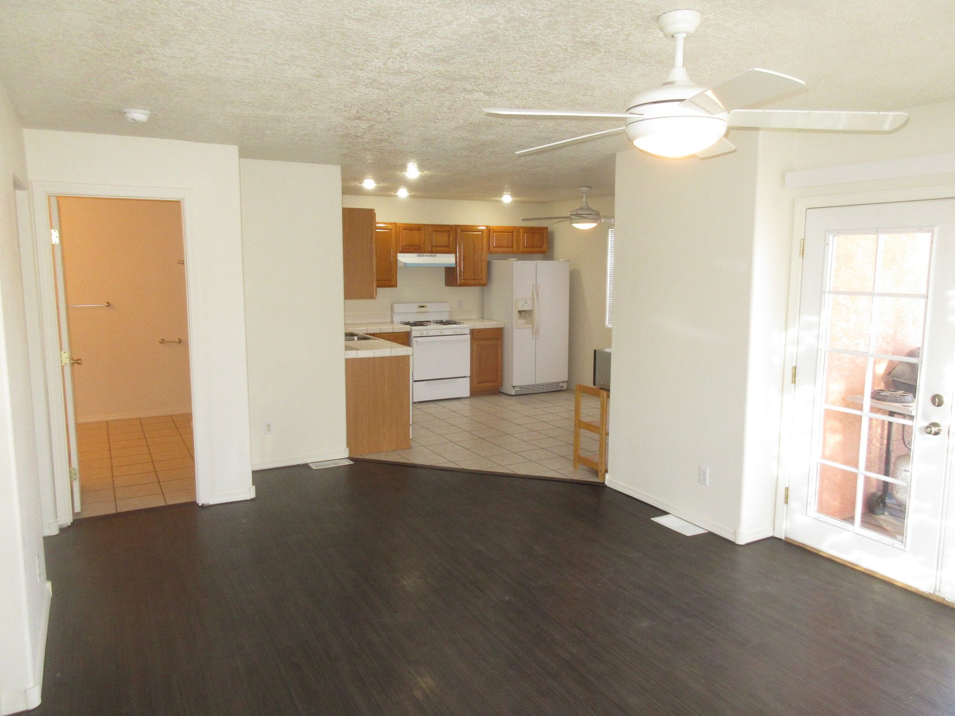 A living room with a ceiling fan and a kitchen in the background