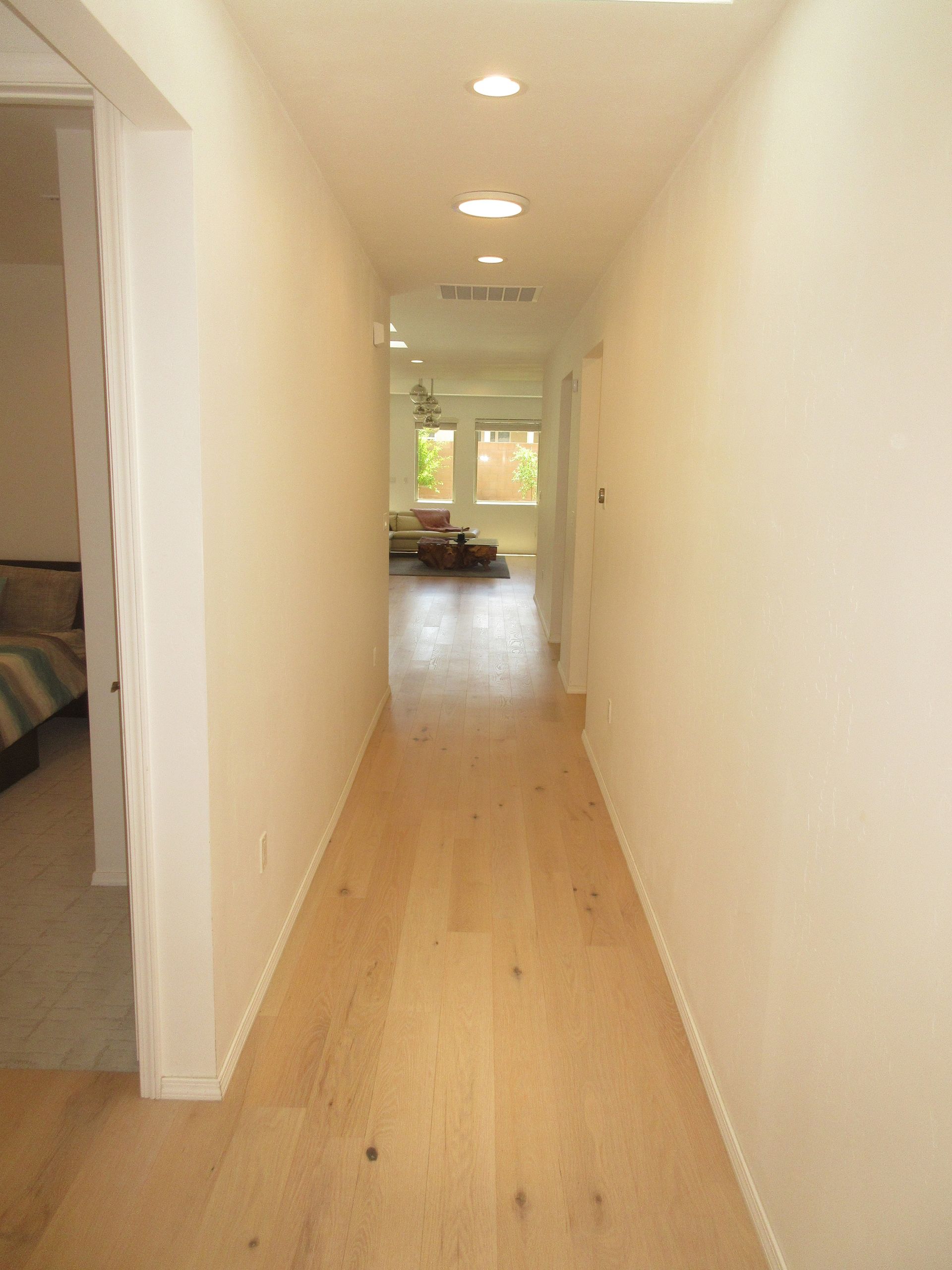 A long hallway with hardwood floors and white walls leading to a living room.