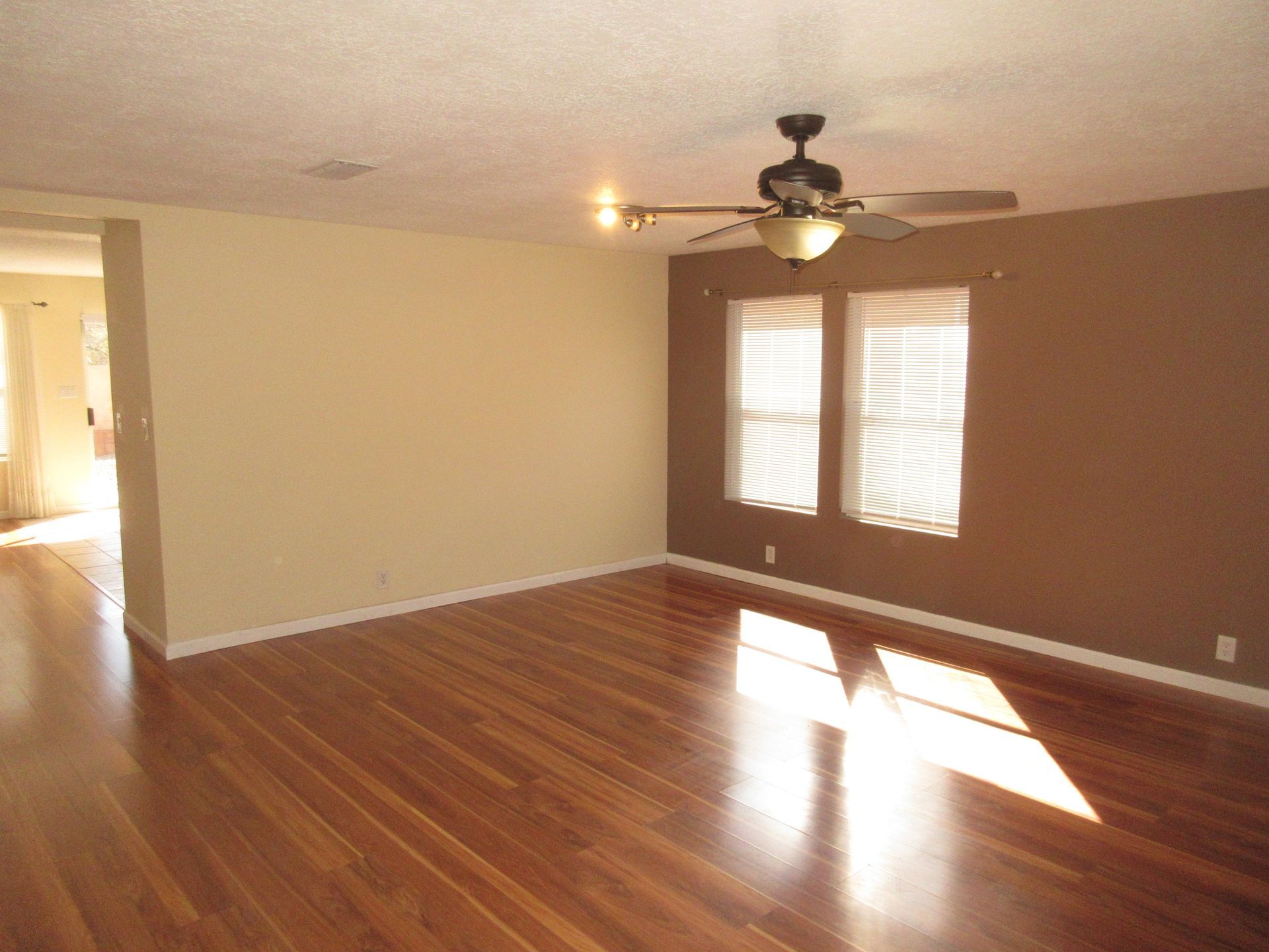 An empty living room with hardwood floors and a ceiling fan