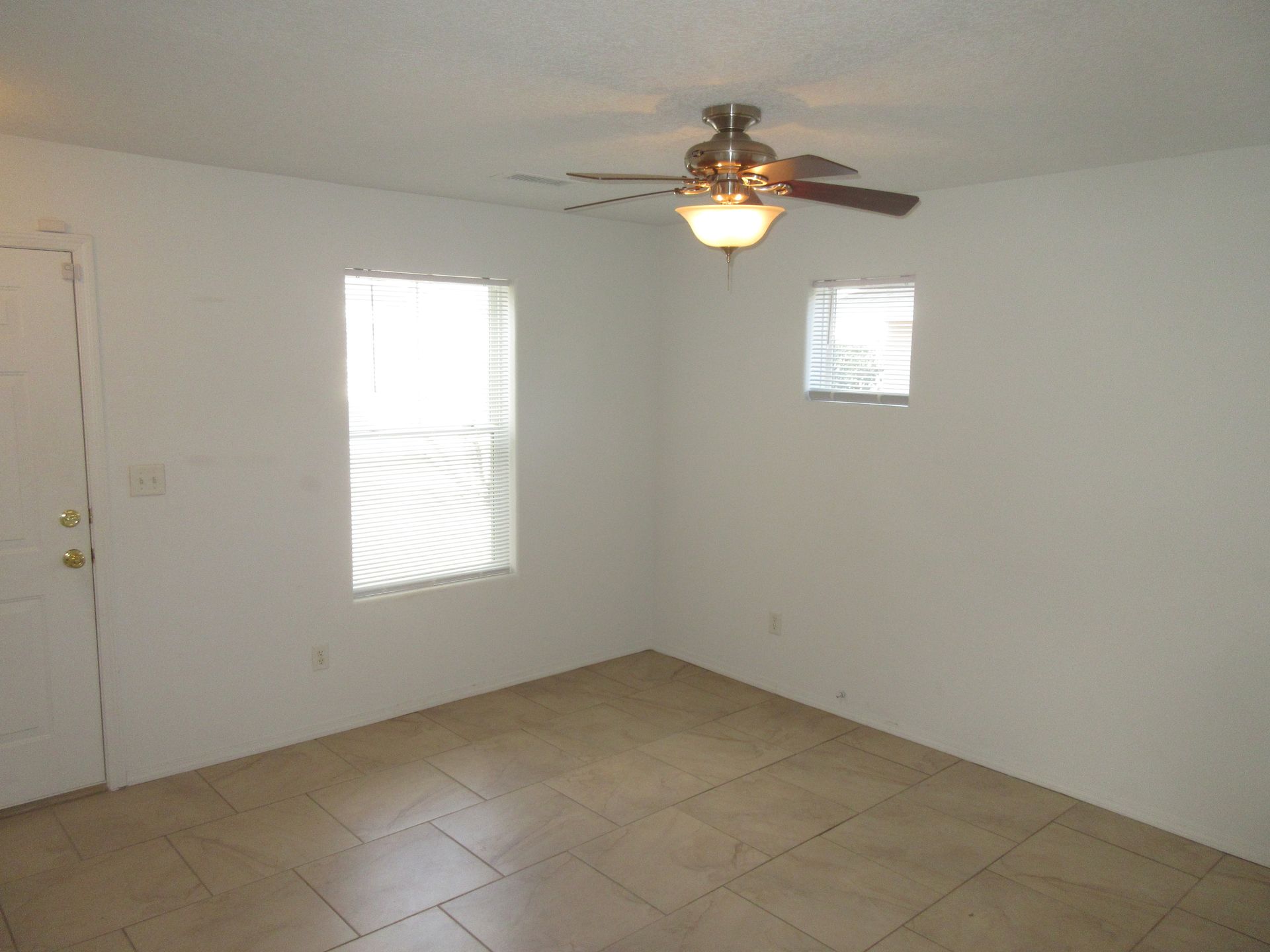 An empty room with a ceiling fan and two windows.