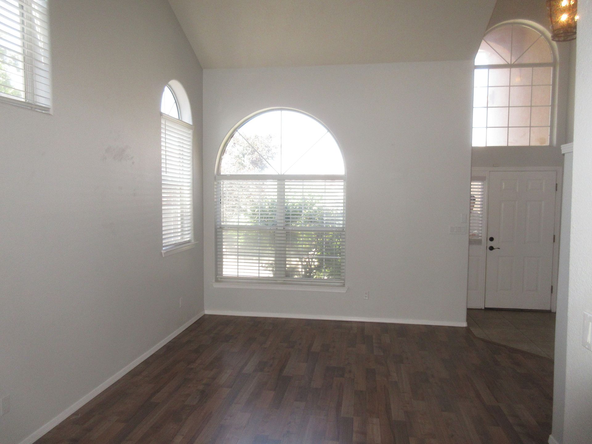 An empty living room with hardwood floors and a large window.