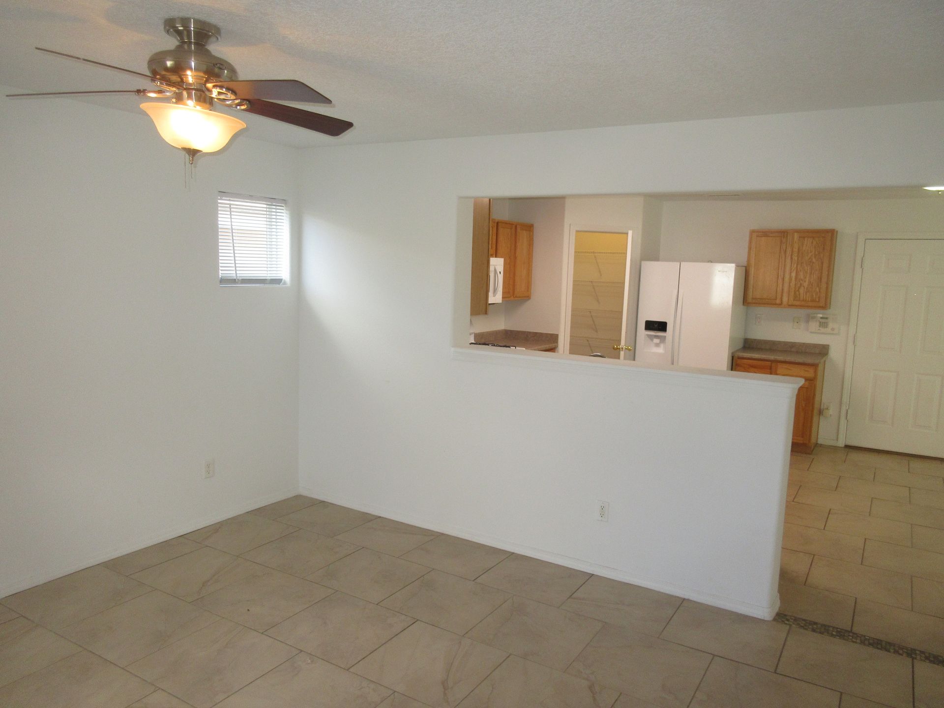 An empty room with a ceiling fan and a refrigerator