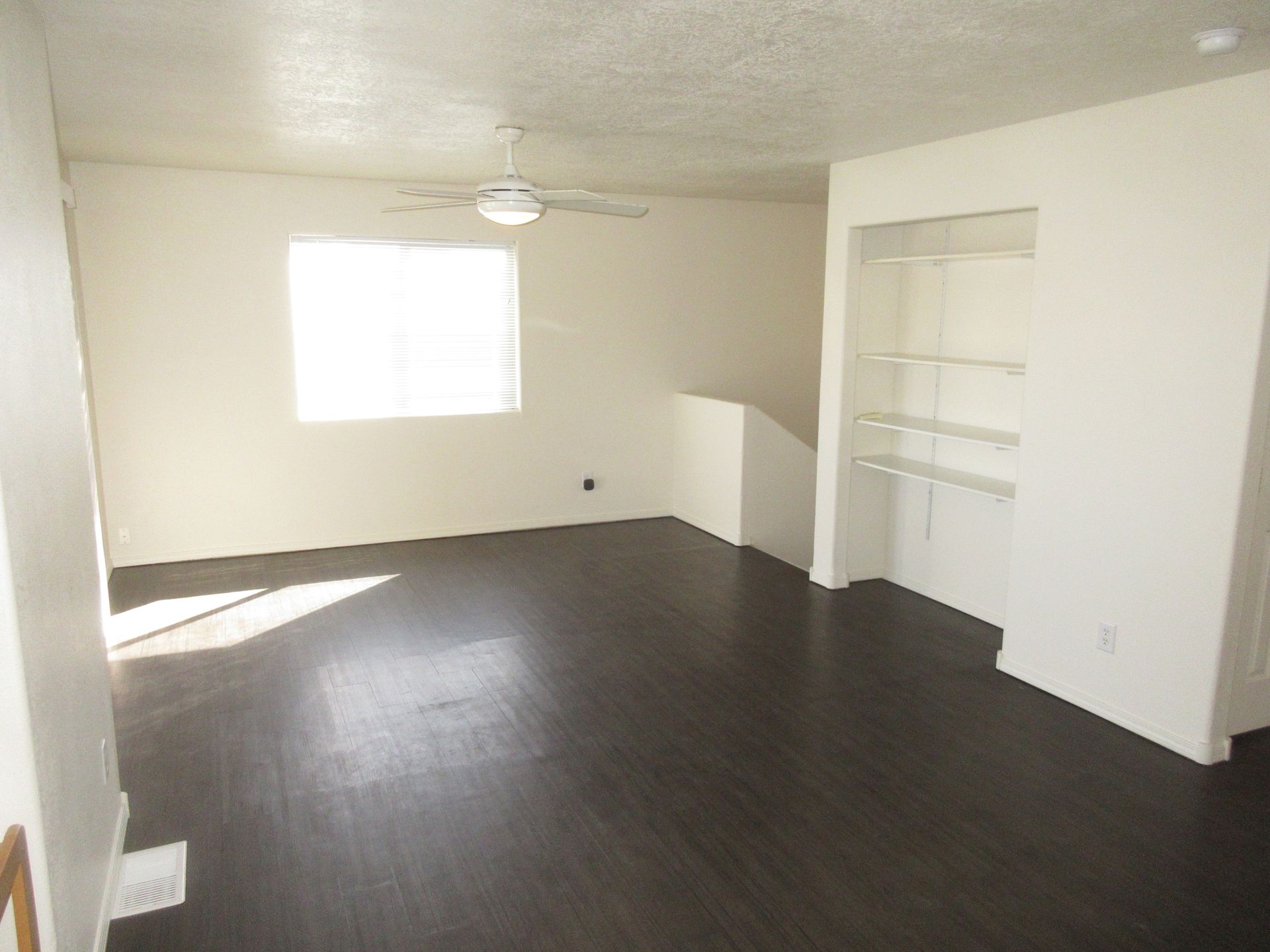 An empty living room with a ceiling fan and a window