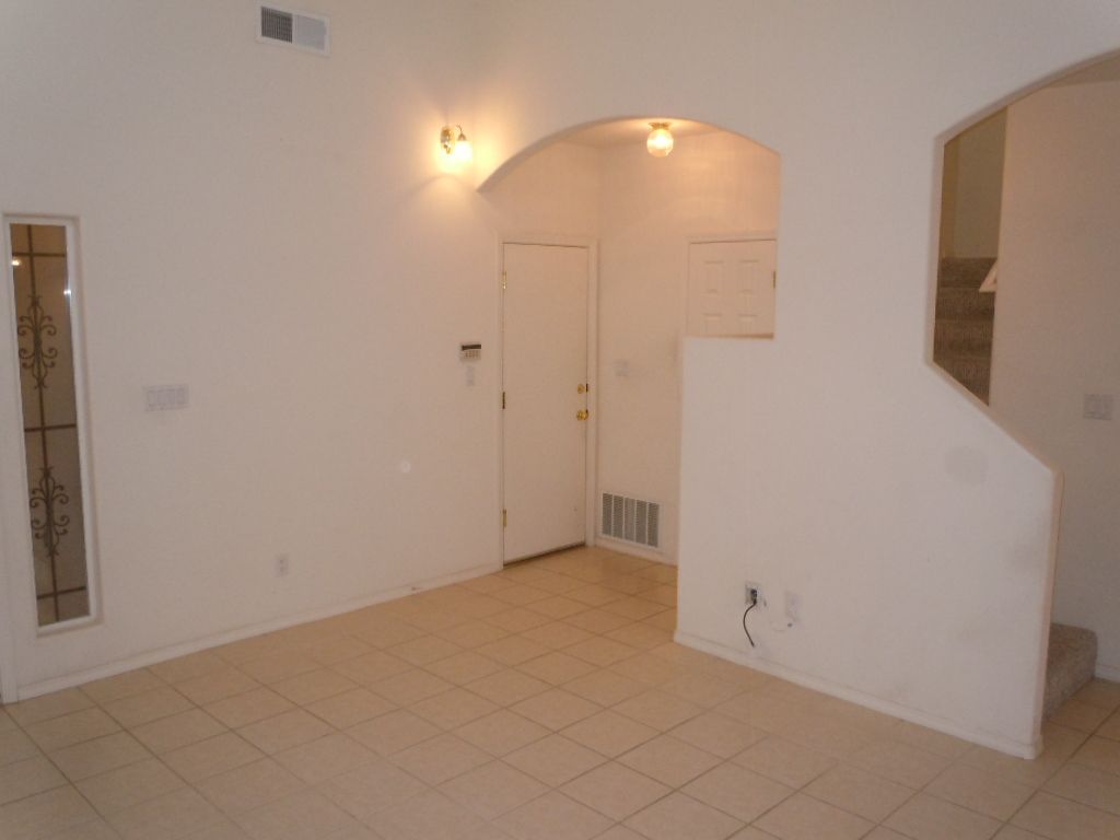 An empty living room with white walls and tile floors